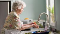 Woman with short hair washes carrots with an electric faucet.
