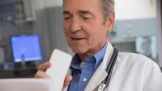 Gray-haired doctor sitting at a monitor and talking into a cell phone