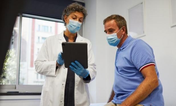 Doctor in mask showing tablet to patient in mask