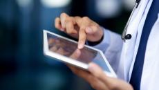 Close up of a doctor, wearing a lab coat and stethoscope, accesses healthcare IT from a tablet.  