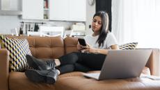 Woman on a couch at home checks her phone to book a doctor's appointment.