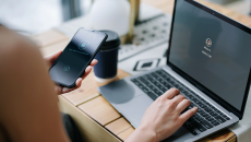An individual is holding her cell phone and logging into her laptop.